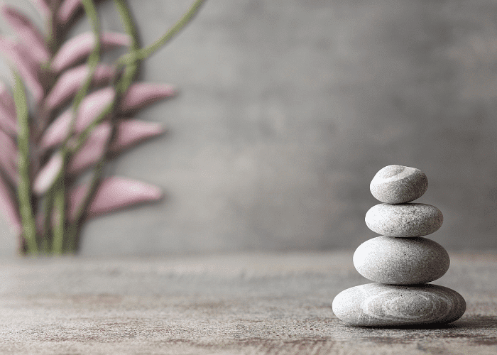 Stacked stones with pink leaves in the background, set against a serene, neutral backdrop.